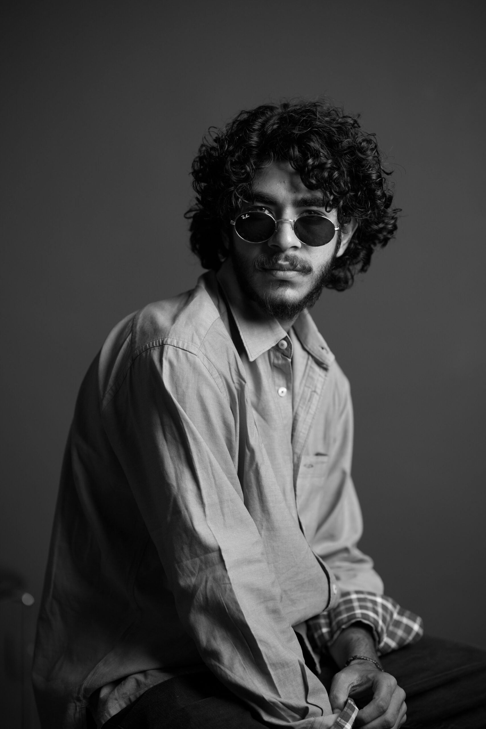 Monochrome portrait of a man with curly hair and sunglasses in a studio.